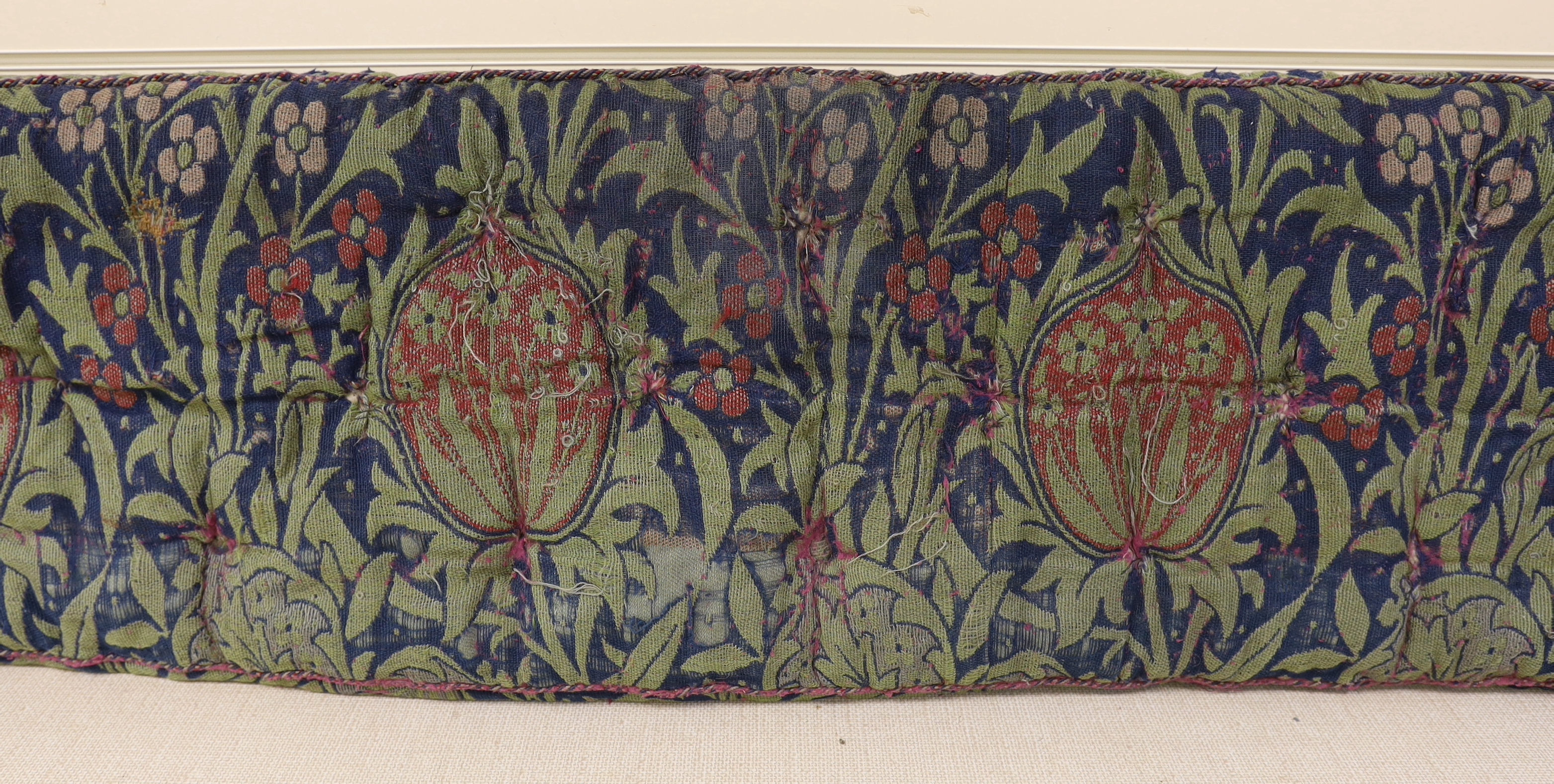 A William Morris Elmore, wool and mohair woven panel by J H Dearle circa 1900, used to cover a buttoned and braided window seat cushion, 196cm wide (at widest point) x 38cm deep, Please note this lot attracts an addition
